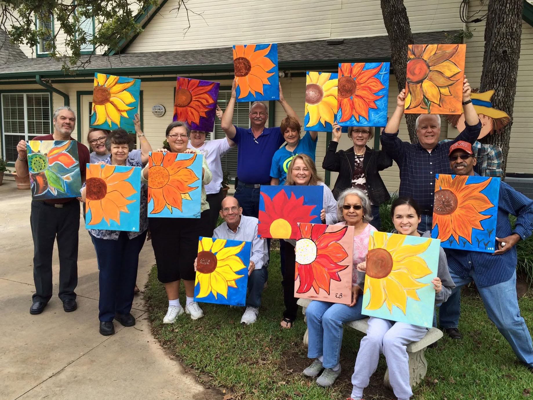 Paint party guests holding their finished sunflower paintings